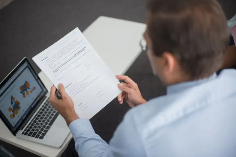 An analyst reviews a printed report next to a laptop showing charts.